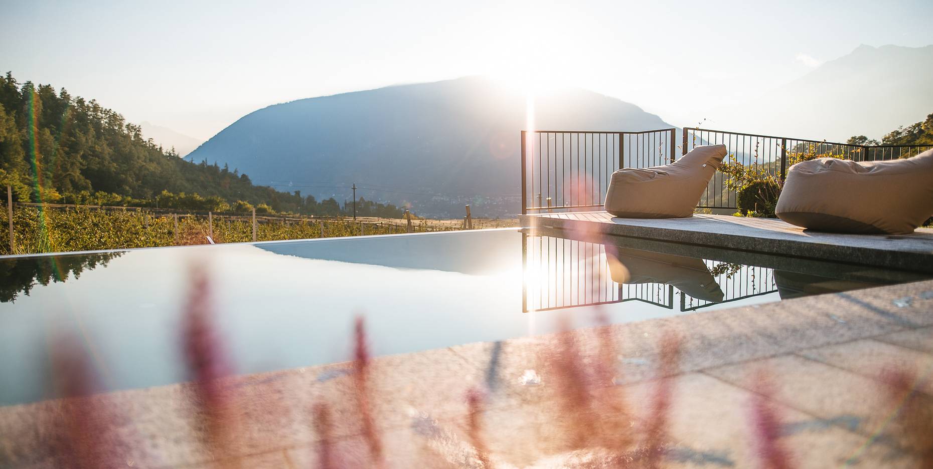 Ein Infinity-Pool auf einer Terrasse mit Sitzsäcken am Beckenrand bei Sonnenuntergang und Blick auf ein Bergpanorama.